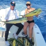 a man and a woman holding mahi-mahi on a fishing boat