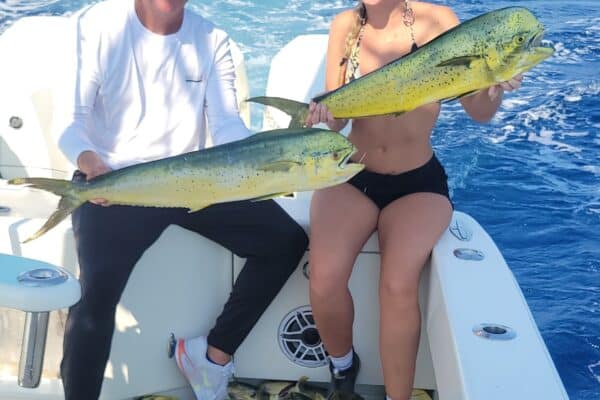 a man and a woman holding mahi-mahi on a fishing boat