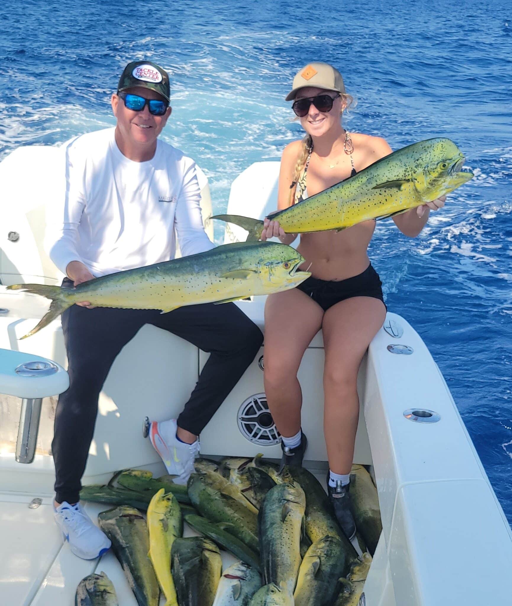 a man and a woman holding mahi-mahi on a fishing boat